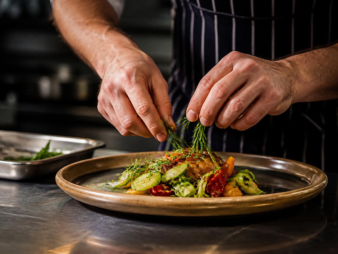 Chef che impiatta verdure fresche ed erbe aromatiche in cucina professionale